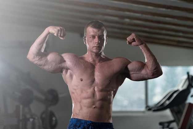 Knappe man staat sterk in de sportschool en buigt spieren Gespierde atletische bodybuilder Fitness Model poseren na oefeningen