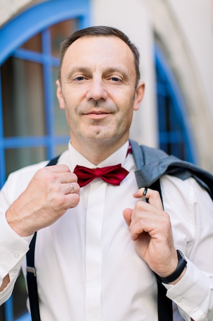 Knappe man van 50 in formele kleding die zijn rode vlinderdas aanpast en naar de camera glimlacht