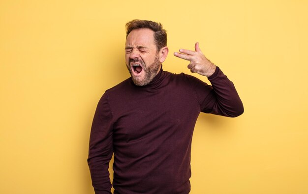 Knappe man van middelbare leeftijd die er ongelukkig en gestrest uitziet, zelfmoordgebaar maakt een pistoolteken met de hand, wijzend naar het hoofd