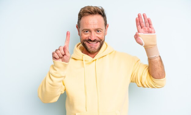 Knappe man van middelbare leeftijd die lacht en er vriendelijk uitziet, met nummer één. gebroken hand concept