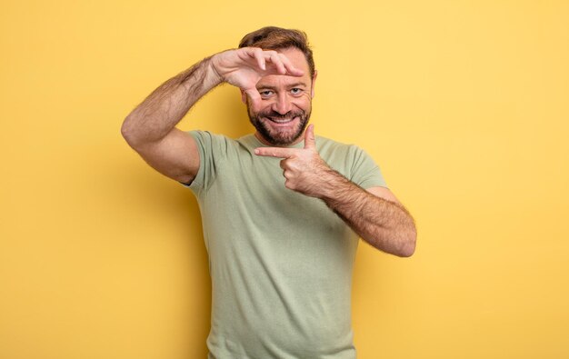 Knappe man van middelbare leeftijd die zich gelukkig, vriendelijk en positief voelt, lacht en een portret of fotolijst maakt met handen