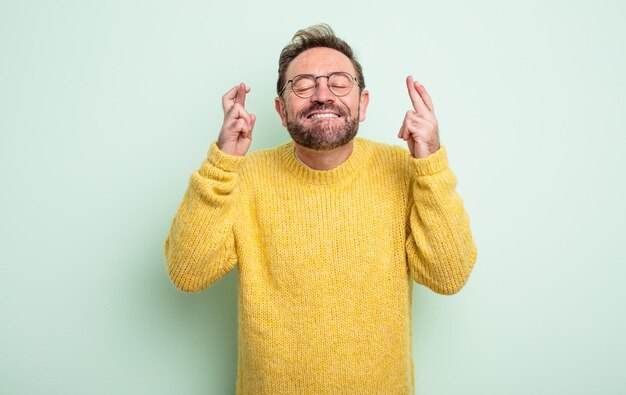 Knappe man van middelbare leeftijd glimlachend en angstig beide vingers kruisend, zich bezorgd voelend en wensend of hopend op geluk