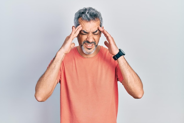 Knappe man van middelbare leeftijd met grijs haar, gekleed in een casual t-shirt met de hand op het hoofd voor pijn in het hoofd vanwege stress. last van migraine.