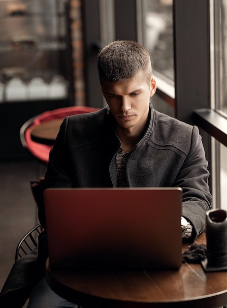 Knappe man zit in een café bij het raam met een laptop