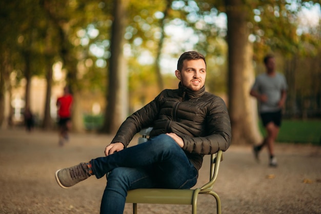 Knappe man zit midden in het park op een kaki krukje