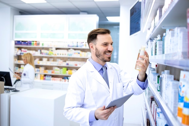 Knappe mannelijke apotheker in witte jas die in apotheekopslag of drogisterij werkt.