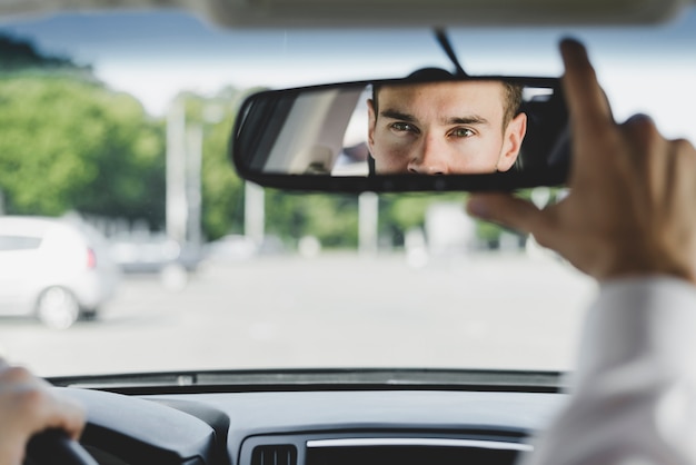 Foto knappe mannelijke bestuurder die de achteruitkijkspiegel in de auto aanpassen