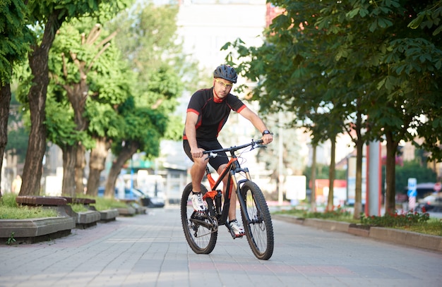 Knappe mannelijke fietser rijden op de fiets langs lege straten van de stad, groene bomen rond. Sportman die ochtend openluchtoefening en opleiding uitvoeren.