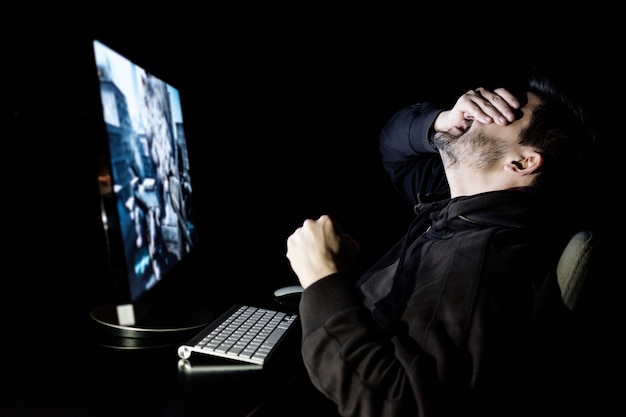 Knappe mannelijke gamer die computervideogame speelt aan de tafel in de donkere kamer