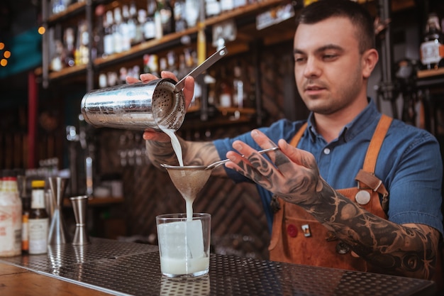 Knappe mannelijke getatoeeerde barman die een drank voorbereiden