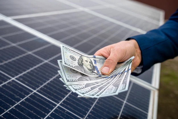 Knappe mannelijke handen met dollars om te betalen voor het werken met zonnepanelen