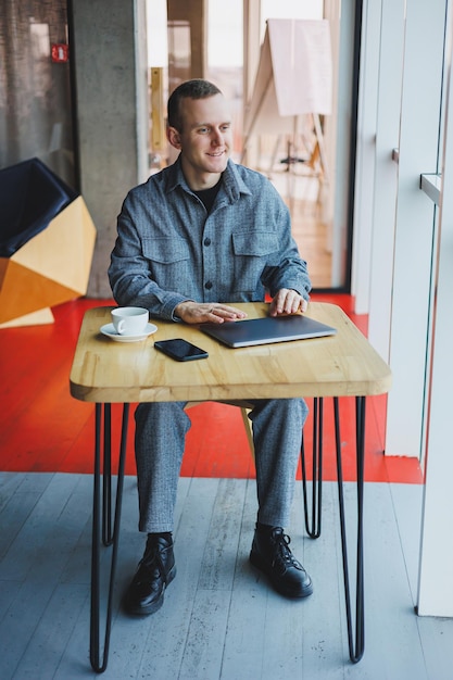 Knappe mannelijke manager zit aan een tafel in een modern kantoor met een gesloten laptop en rust op afstand werken