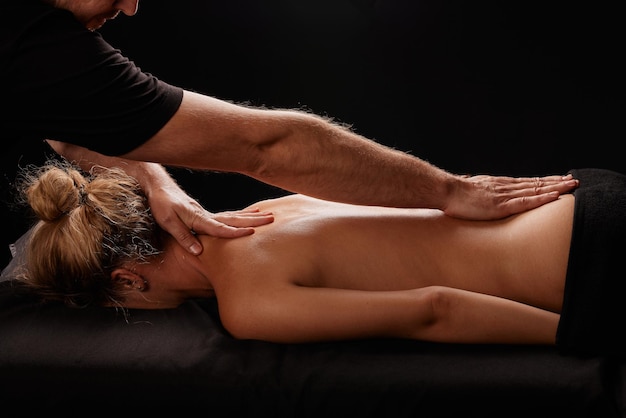 knappe mannelijke masseur die een meisje massageert op een zwarte achtergrond concept van therapeutische ontspannende massage