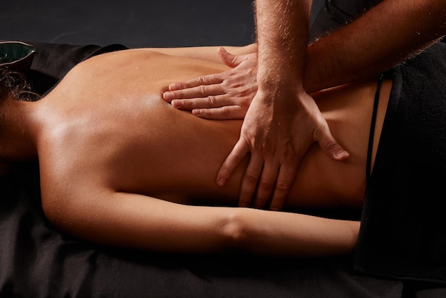 Foto knappe mannelijke masseur die een meisje masseert op een zwarte achtergrond concept van therapeutische ontspannende massage