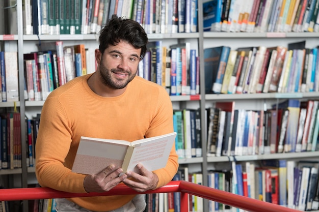 Knappe mannelijke student met boeken die in een middelbare schoolbibliotheek werken