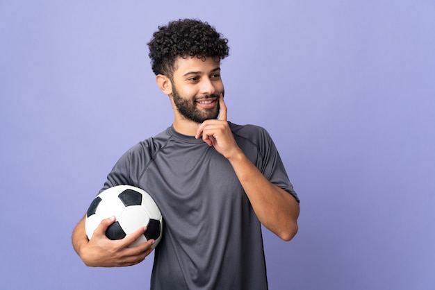 Knappe marokkaanse jonge voetballer man meer dan geïsoleerd op paarse muur een idee denken tijdens het opzoeken