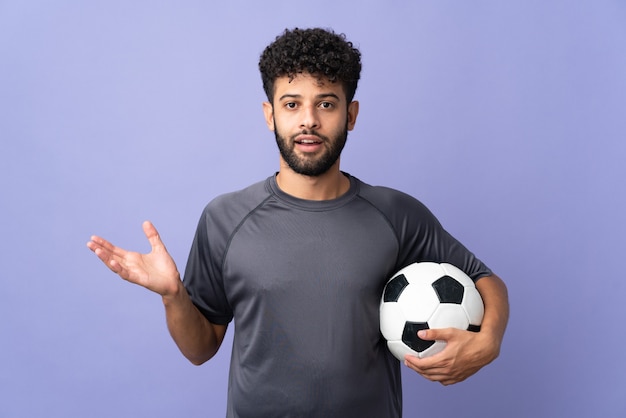 Knappe Marokkaanse jonge voetballer man meer dan geïsoleerd op paarse muur met geschokte gezichtsuitdrukking