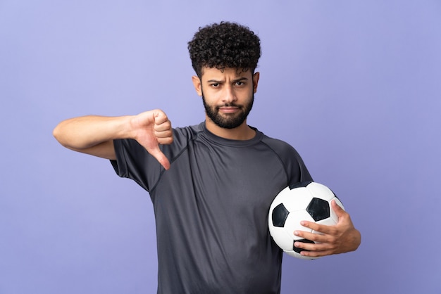 Knappe Marokkaanse jonge voetballer man op geïsoleerd op paars met duim omlaag met negatieve uitdrukking