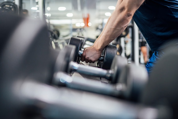 Knappe mens die bodybuilding gewichten in gymnastiek uitoefenen