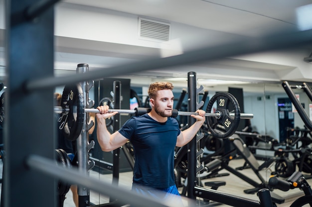 Knappe mens die bodybuilding gewichten in gymnastiek uitoefenen