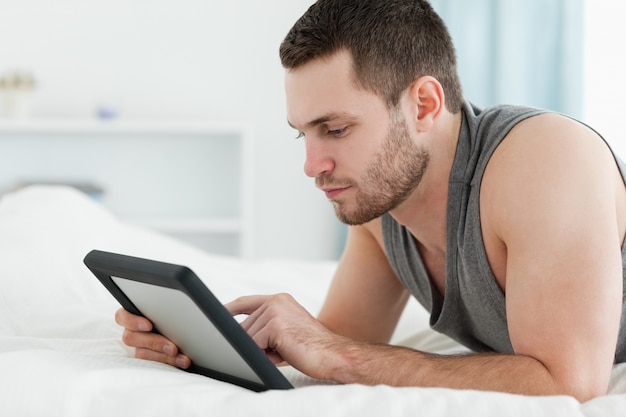 Knappe mens die een tabletcomputer met behulp van terwijl het liggen op zijn buik