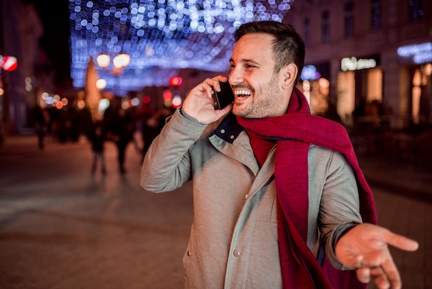 Knappe mens die terwijl het spreken op mobiele telefoon bij nacht in verfraaide stadsstraat lachen.