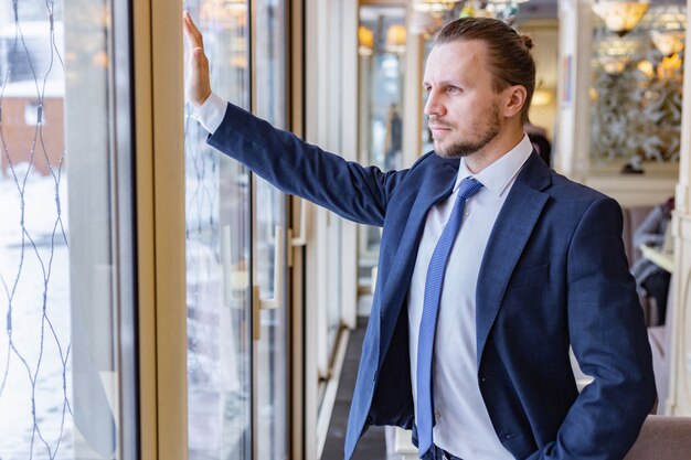 Knappe mens in het en pak die zich ernstig in het venster bevinden binnen bevinden zich