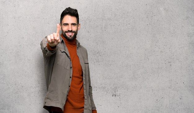 Knappe mens met baard die en een vinger over geweven muur tonen opheffen