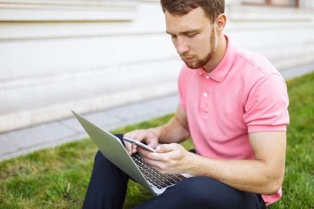 Knappe mensenzitting op het gras in de stad met laptop, baanonderzoek