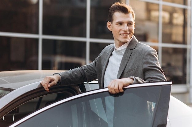 Knappe moderne jonge man die zijn auto binnenkomt terwijl hij buiten staat