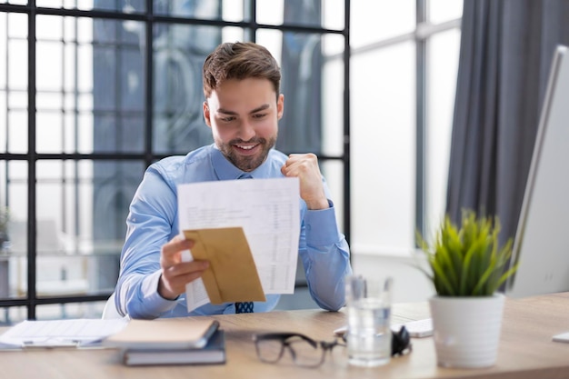 Knappe ondernemer leest een brief uit een envelop op een desktop op kantoor