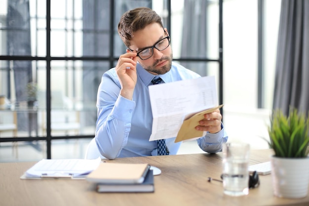 Knappe ondernemer leest een brief uit een envelop op een desktop op kantoor