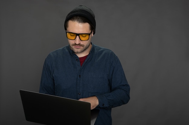 Knappe ongeschoren man die met laptop aan de grijze studio achtergrond kopie ruimte werkt