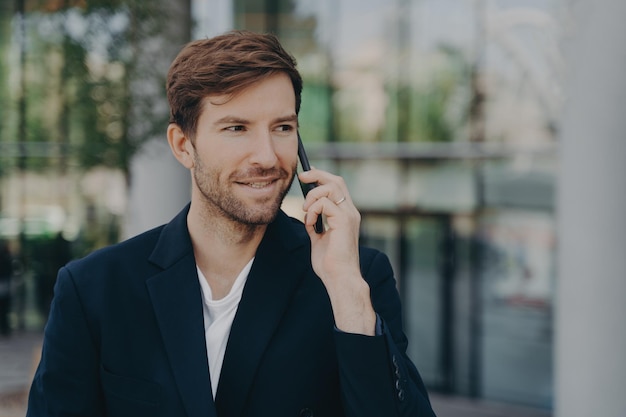 Knappe ongeschoren mannelijke uitvoerende werknemer verliet zakelijke bouwgesprekken via smartphone