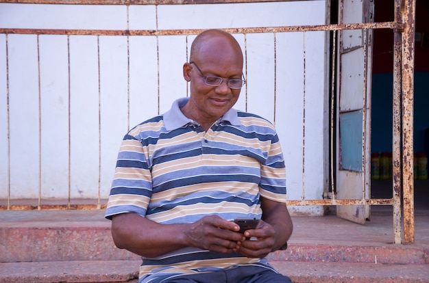 Knappe oudere afrikaanse man die stripkleding draagt, voelt zich opgewonden over wat hij op zijn telefoon zag.