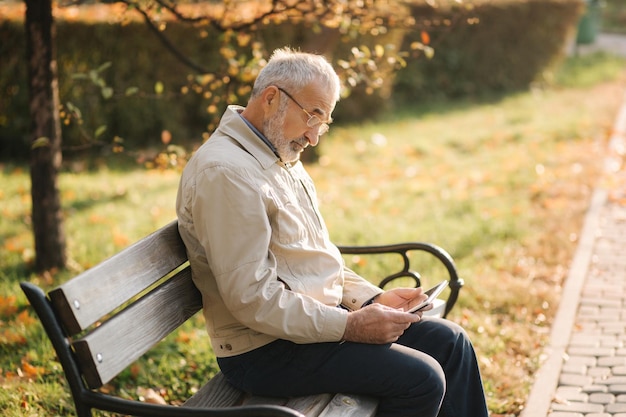 Knappe oudere man zittend op de bank en tablet gebruiken om te scrollen op internet