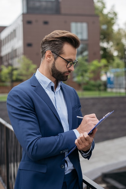 Knappe peinzende zakenman met klembord schrijven analyseren van documenten planning project