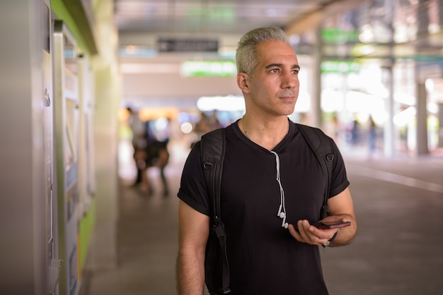 Knappe Perzische man met grijs haar met behulp van telefoon op het treinstation van de hemel