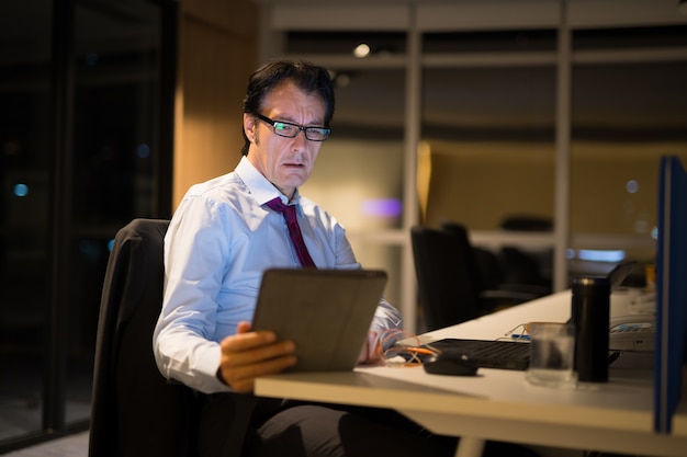 Knappe rijpe zakenman zitten en werken in kantoor 's nachts