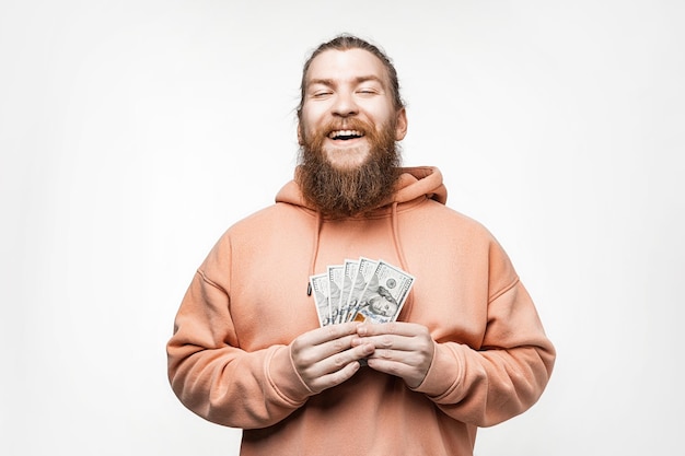 Knappe Scandinavische gelukkig man met dollar valuta geld in zijn handen op grijze achtergrond man met gember kapsel en baard in een sweatshirt het concept van geld salaris financiën investering