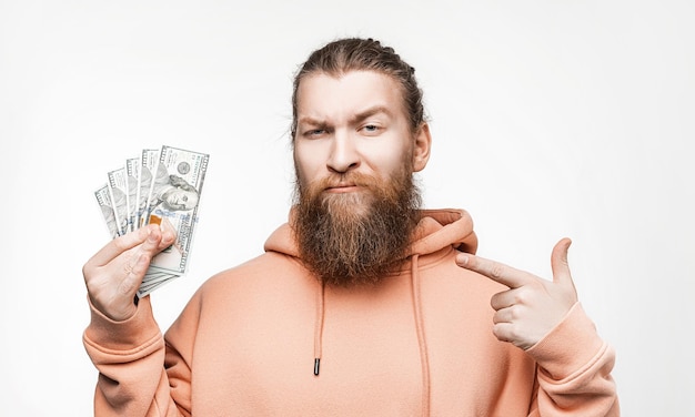 Knappe Scandinavische man met dollar valuta geld in zijn handen op grijze achtergrond man met gember kapsel en baard in een sweatshirt het concept van geld salaris financiën investering