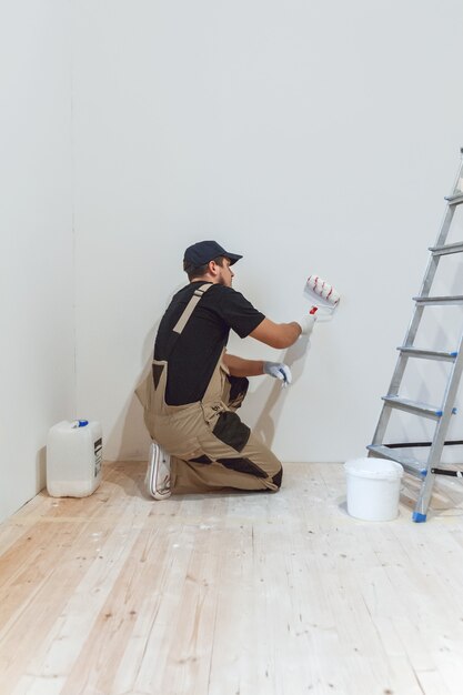 Knappe schilder met verfroller in lege ruimte schildert de muur