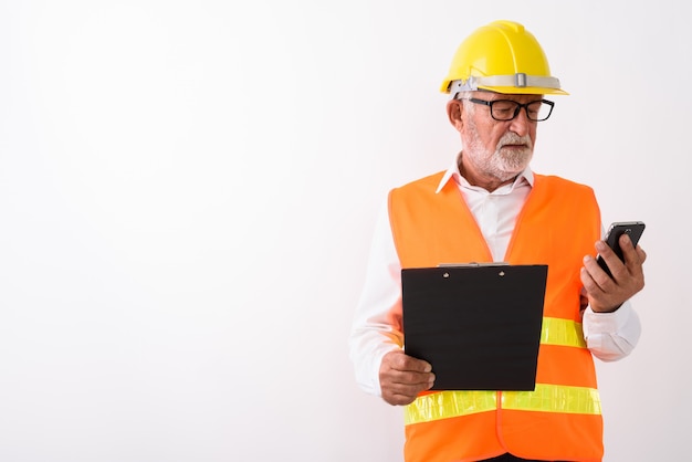 knappe senior bebaarde man bouwvakker met behulp van mobiele telefoon terwijl klembord en het dragen van een bril op wit