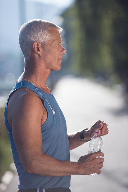 knappe senior joggende man die na het hardlopen vers water uit de fles drinkt