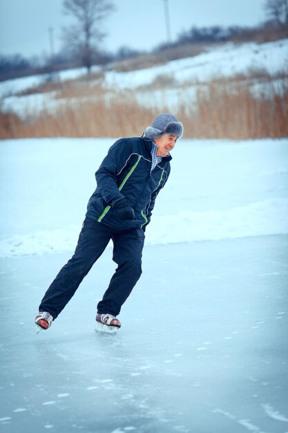 Knappe senior man in de zonnige winter natuur gaan schaatsen.