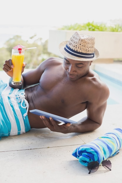 Knappe shirtless man met behulp van tablet pc bij het zwembad met cocktail