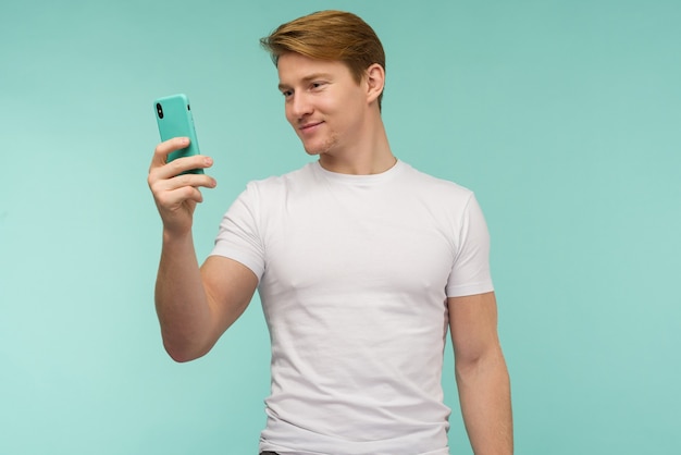 Knappe sportieve roodharige man in wit t-shirt neemt een selfie of zendt online uit op een smartphone