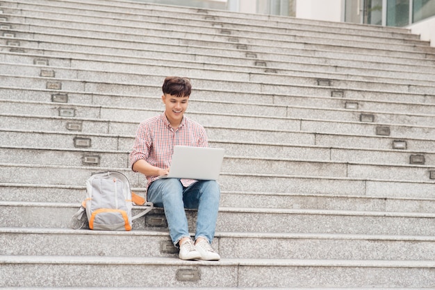 Knappe student in hemd die op laptop werkt die op de trap zit op de universiteit