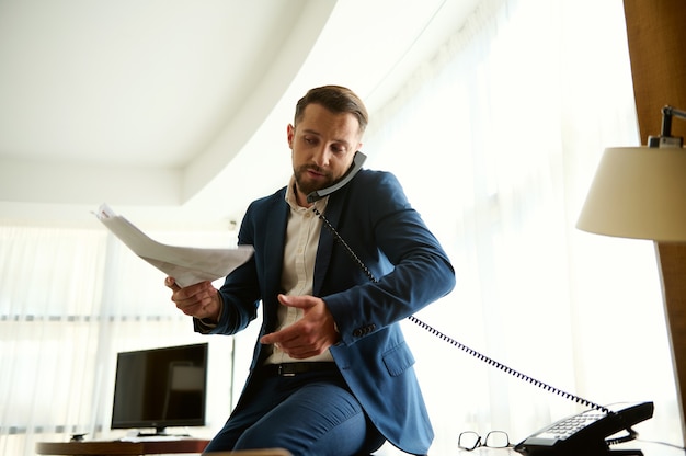 Knappe succesvolle zakelijke investeerder, CFO, financieel directeur, investeringsadviseur, praten op vaste telefoon met een stapel documenten voor ondertekening. Zakelijk, onderhandelingen, communicatieconcepten