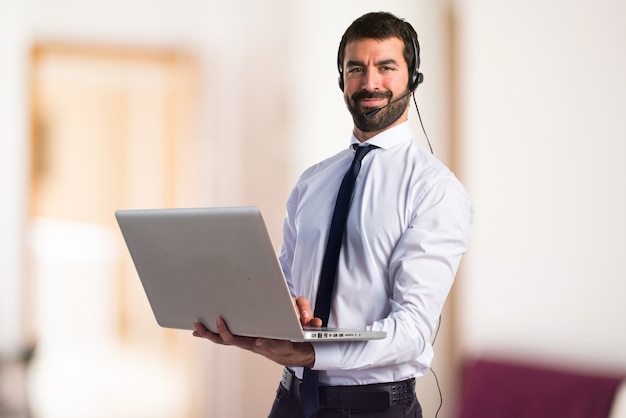 Knappe telemarketing man met laptop op ongerichte achtergrond